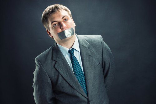 Standing man with mouth and hands covered by duct tape preventing speech,
