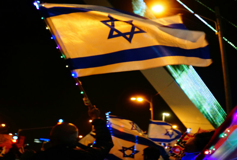 Individual waving Israeli flag at night in Jerusalem.