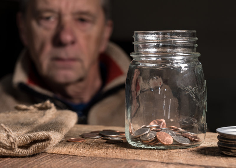 Depressed senior man looking at empty glass savings jar