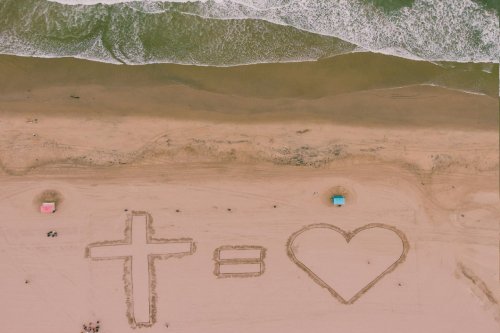Image imprinted into the sand of a beach of a Christian cross equals a heart or love