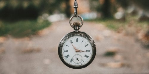 Pocket watch being held by its chain outdoors