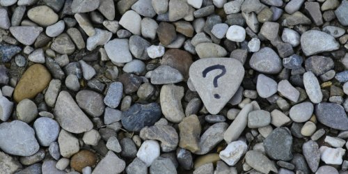 Stones on a beach, one stone has a question mark written on it