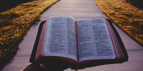 man walking with an open Bible down a road at sunset
