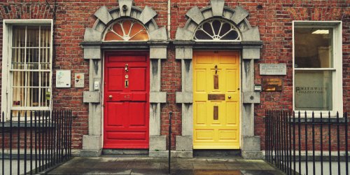 Two doors on an old house block in Ireland. One door is red and the door on the right is yellow.